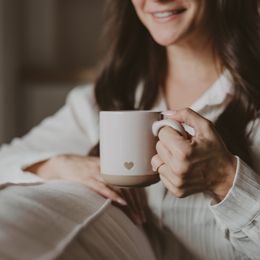 Person holding a mug with a heart design, wearing a white shirt.