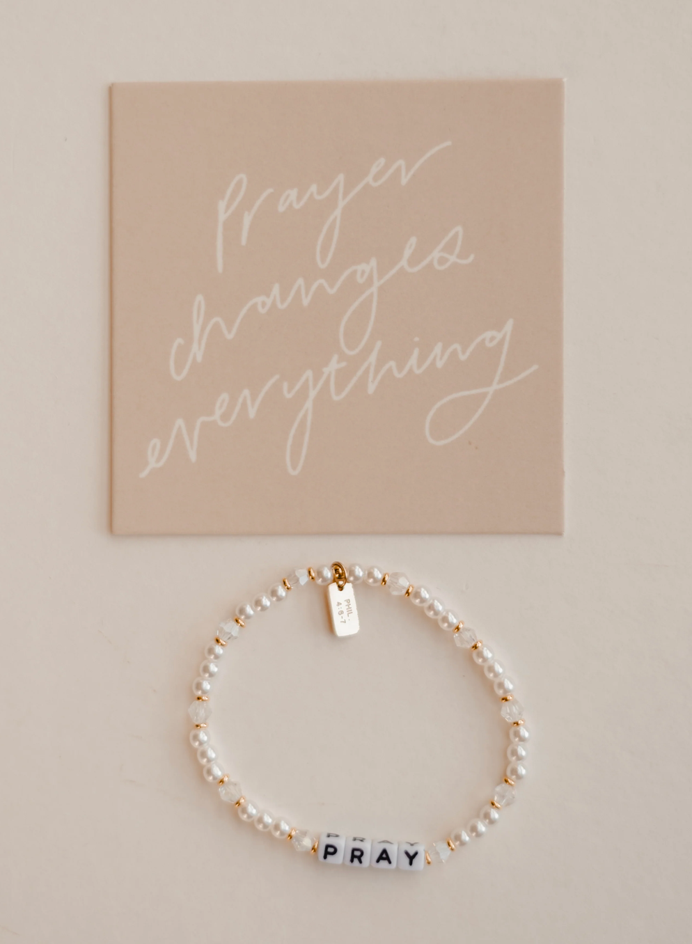 Bracelet with 'PRAY' charm on a beige background with motivational quote