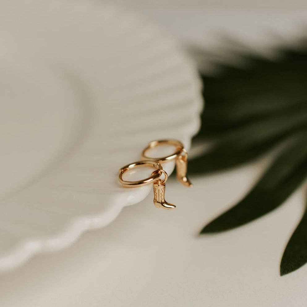 Gold boot-shaped ring on a white fabric background with green leaves