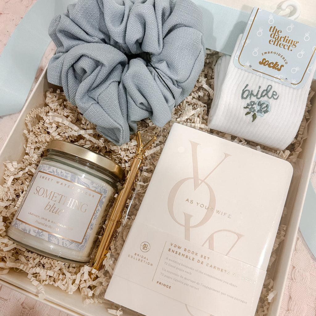 Curated bride-to-be gift box featuring a Something Blue soy candle, embroidered bride socks, powder blue jumbo scrunchie, gold diamond pen, and keepsake vow books, beautifully arranged in a cream magnetic gift box with crinkle paper.