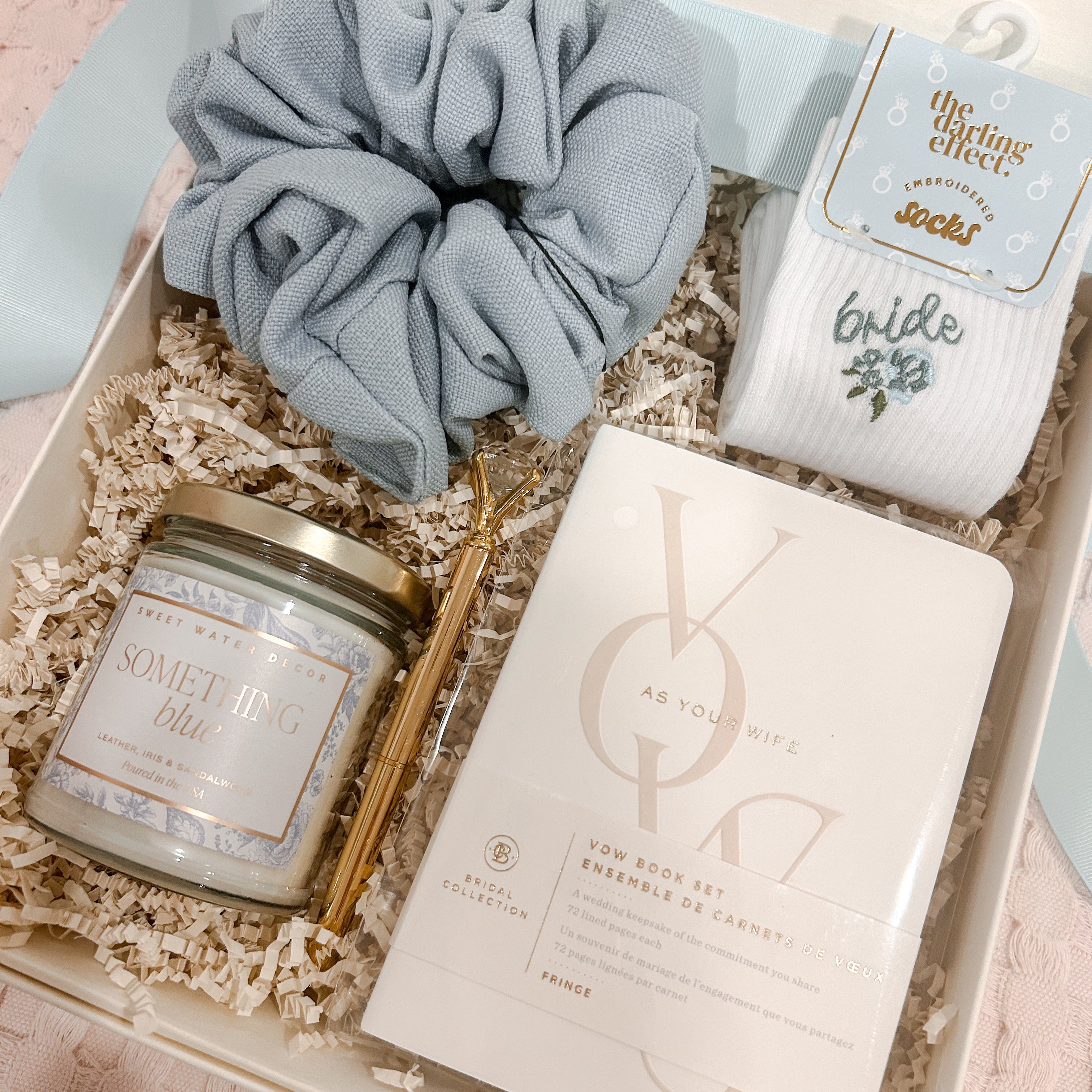 Curated bride-to-be gift box featuring a Something Blue soy candle, embroidered bride socks, powder blue jumbo scrunchie, gold diamond pen, and keepsake vow books, beautifully arranged in a cream magnetic gift box with crinkle paper.