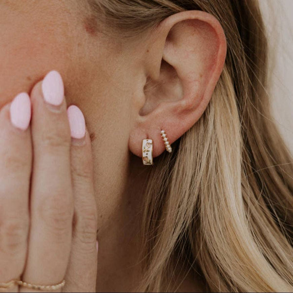 Close-up of an ear wearing a gold hoop earring with a blurred background