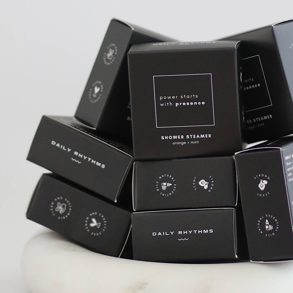Stack of black 'Daily Rhythms' shower steamers on a white marble surface