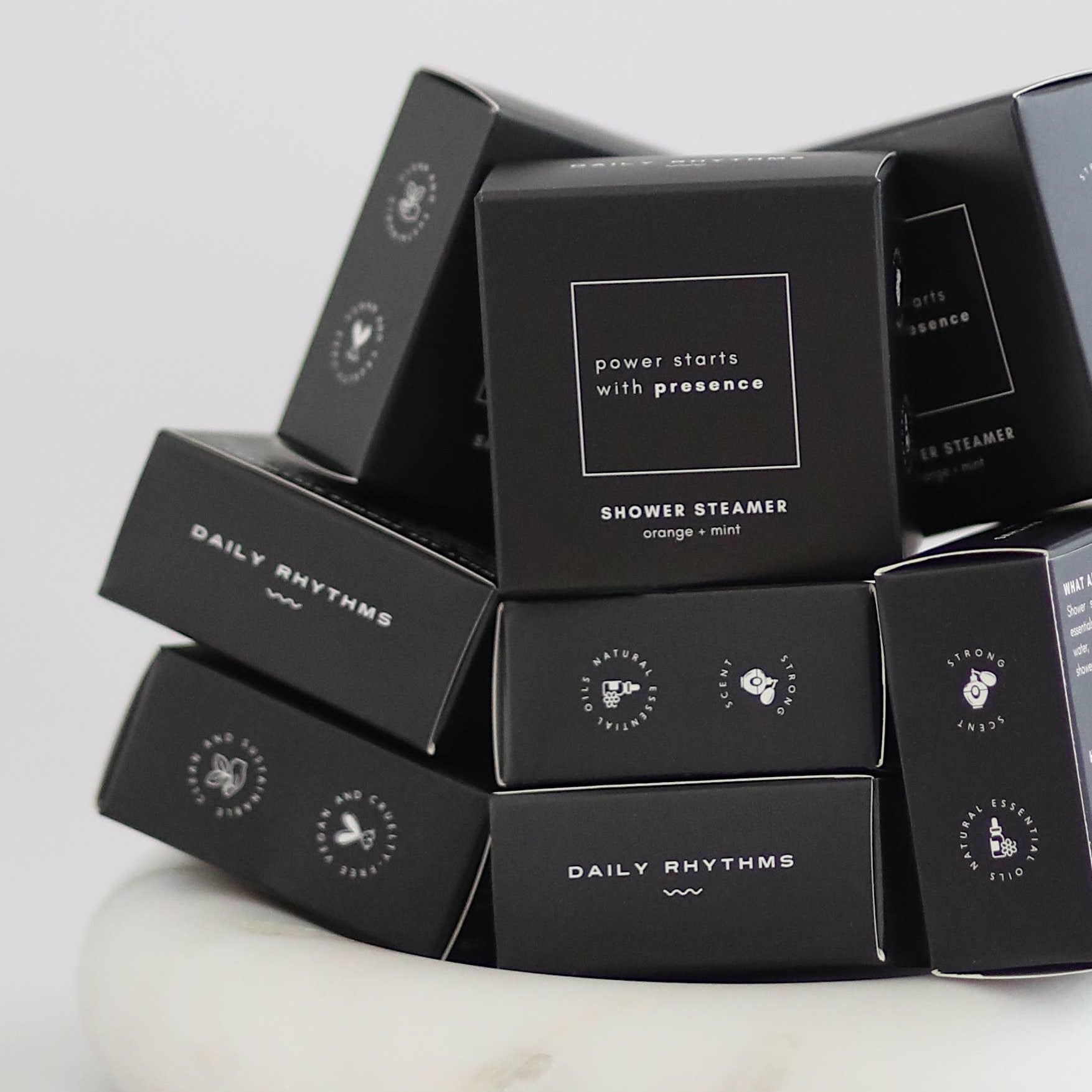 Stack of black 'Daily Rhythms' shower steamers on a white marble surface