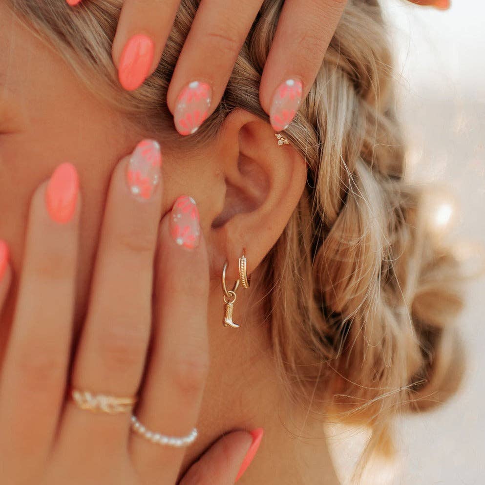 Close-up of a person's hand with pink nail polish and gold jewelry, touching their hair.