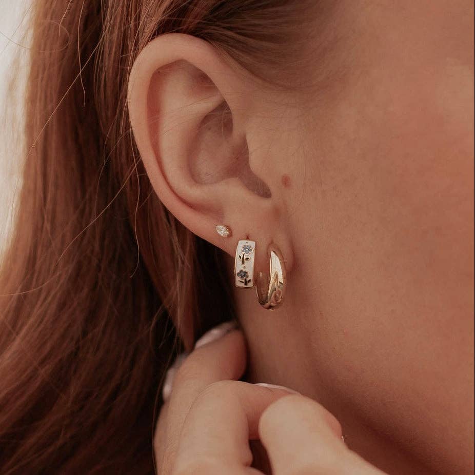Close-up of an ear wearing gold hoop earrings with a blurred background