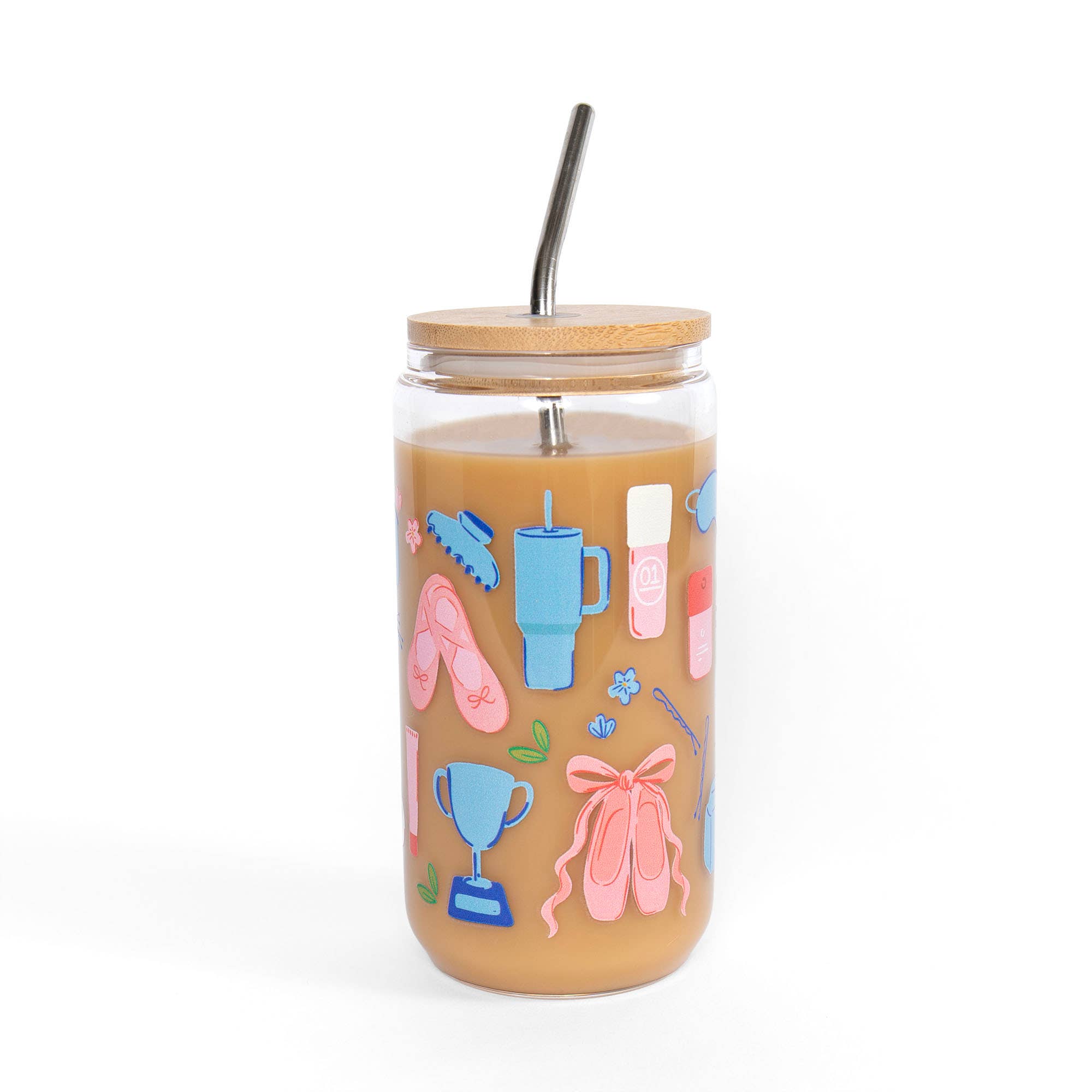 A clear glass tumbler with a light wood lid and black metal straw, filled with an orange-brown beverage and decorated with colorful illustrations of ballet shoes, a trophy, a blue cup, and a ribbon.