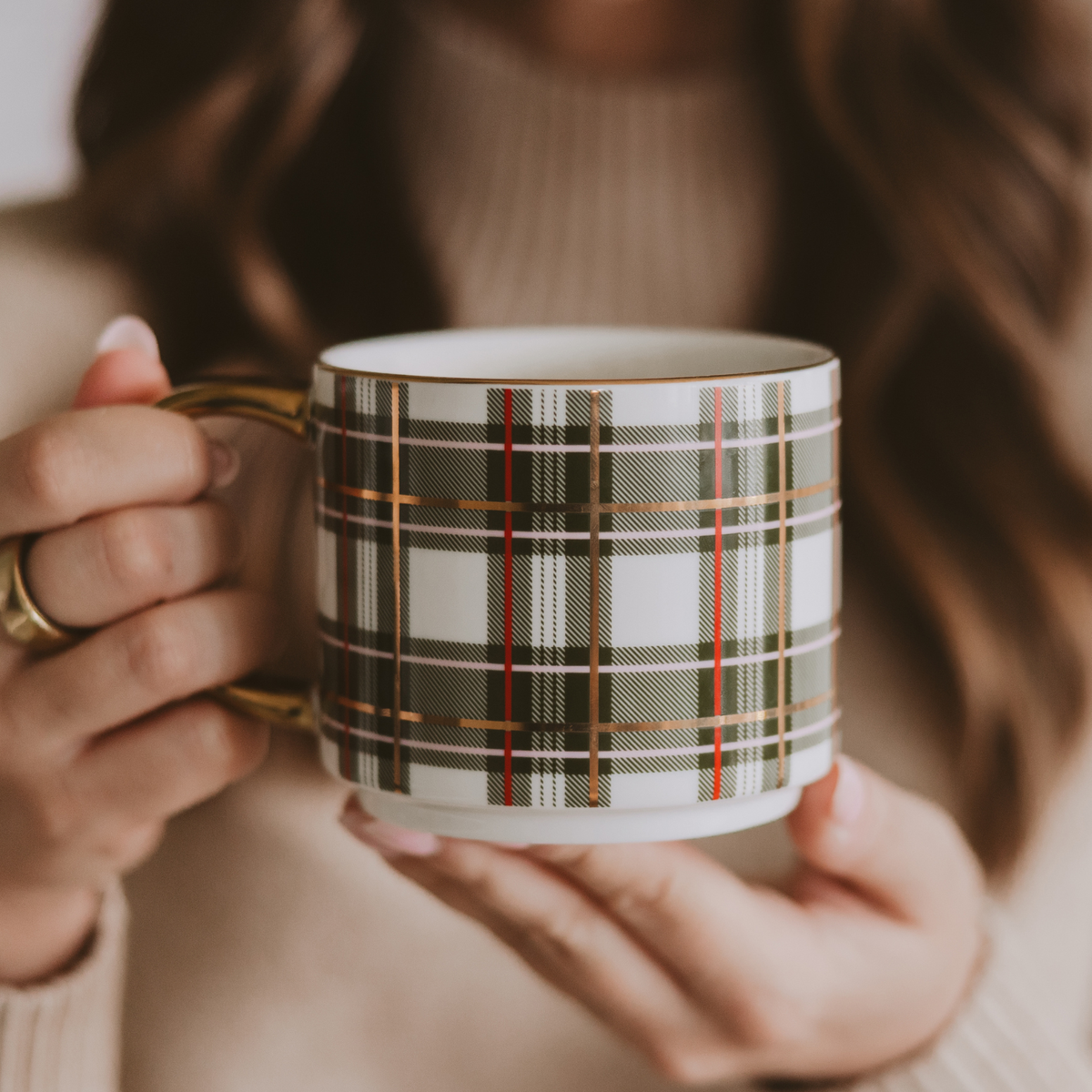 Person holding a green plaid coffee mug with red stripes, gold accents, and a gold handle.
