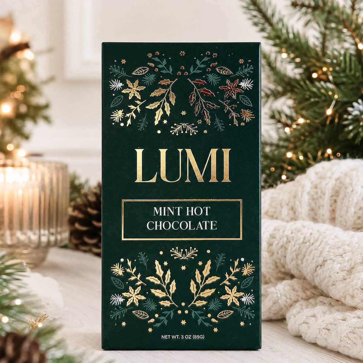 A tall rectangular box of Lumi Mint Hot Chocolate stands upright on a tabletop. The box is dark green with gold floral illustrations and gold lettering.