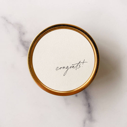 Round white card with 'congrats!' on a gold border against a marble background