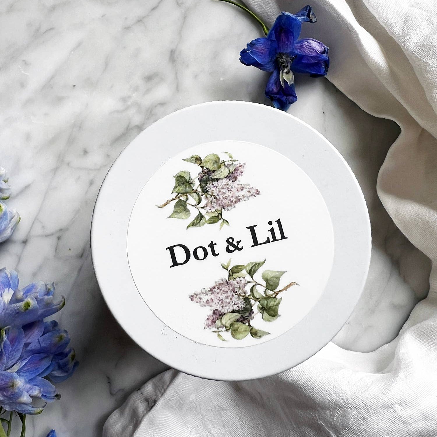 White container with floral design and 'Dot & Lil' text on a marble surface with flowers.