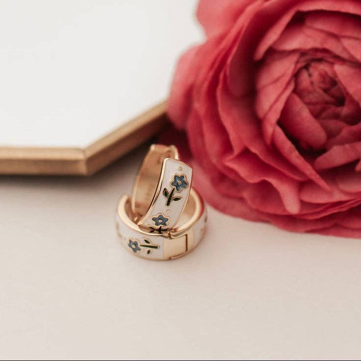 Gold ring with floral design next to a pink rose on a light background