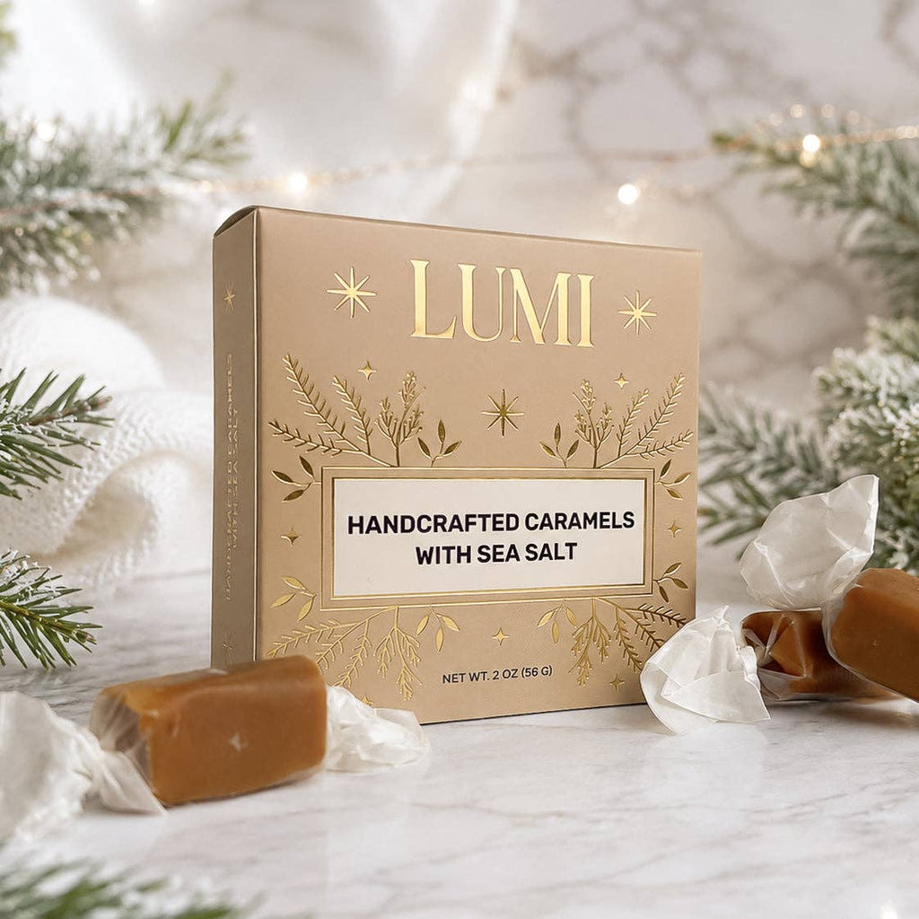 A box of LUMI Handcrafted Caramels with Sea Salt sits on a marble surface surrounded by wrapped caramel candies and festive greenery.