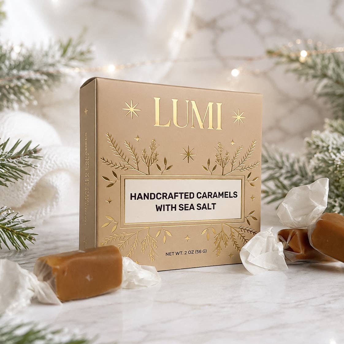 A box of LUMI Handcrafted Caramels with Sea Salt sits on a marble surface surrounded by wrapped caramel candies and festive greenery.