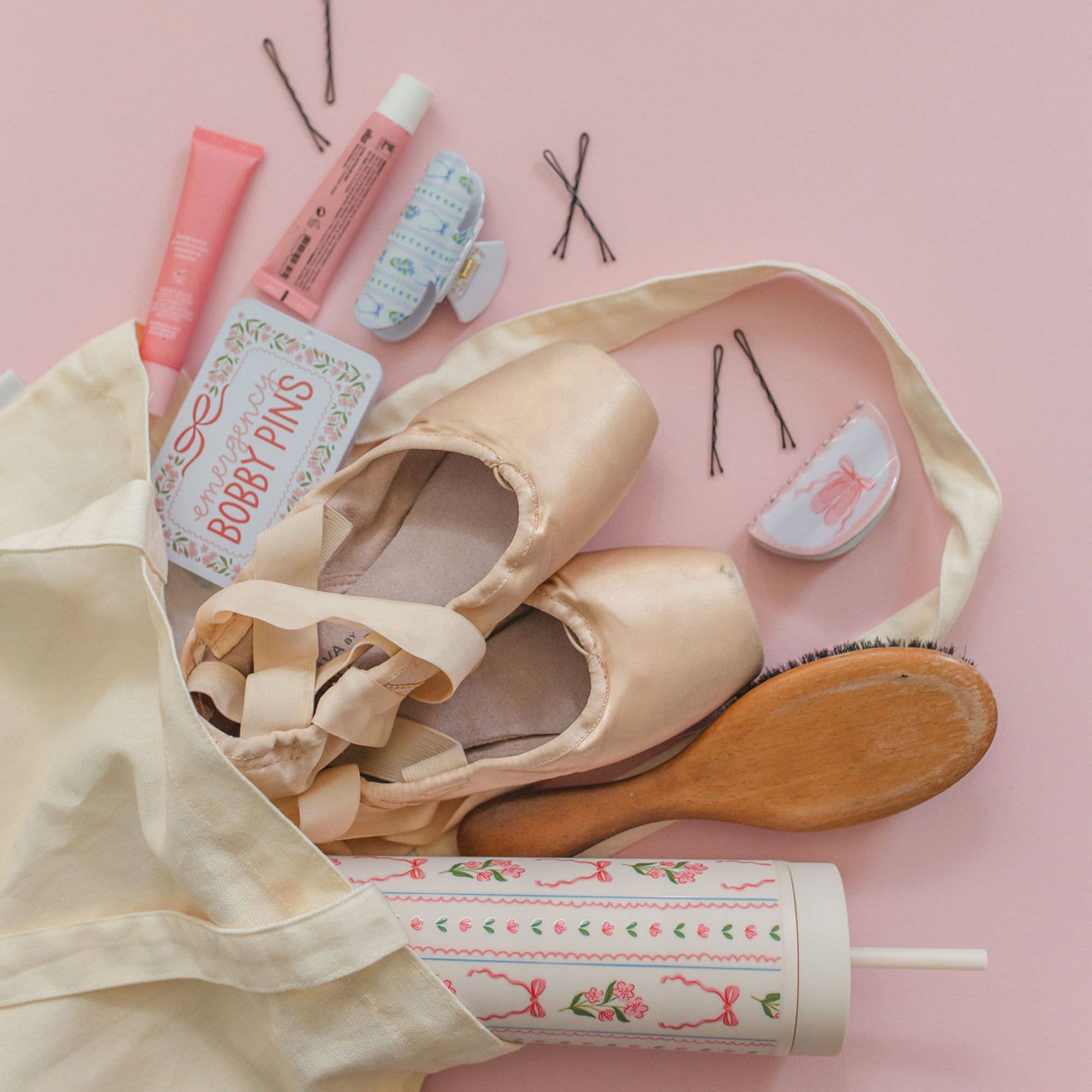 Ballet shoes with hair accessories and beauty products on a pink background