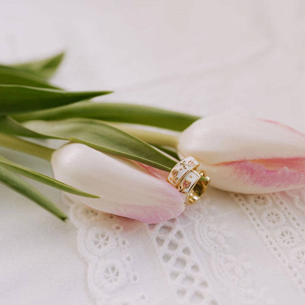 Gold ring on a pink tulip with green leaves on a white lace background