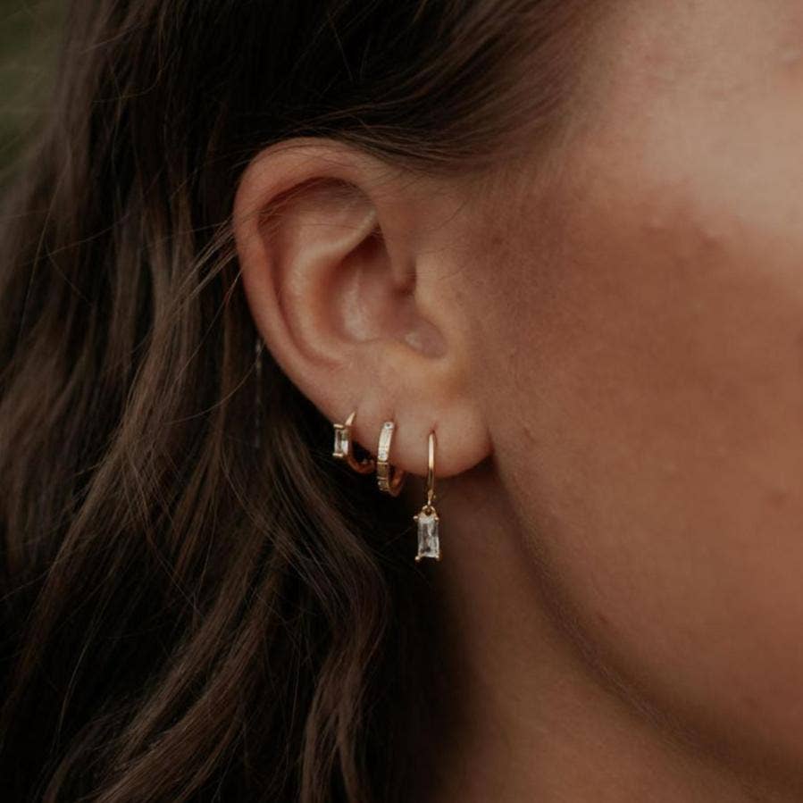 Close-up of an ear wearing gold hoop earrings with small gemstones.