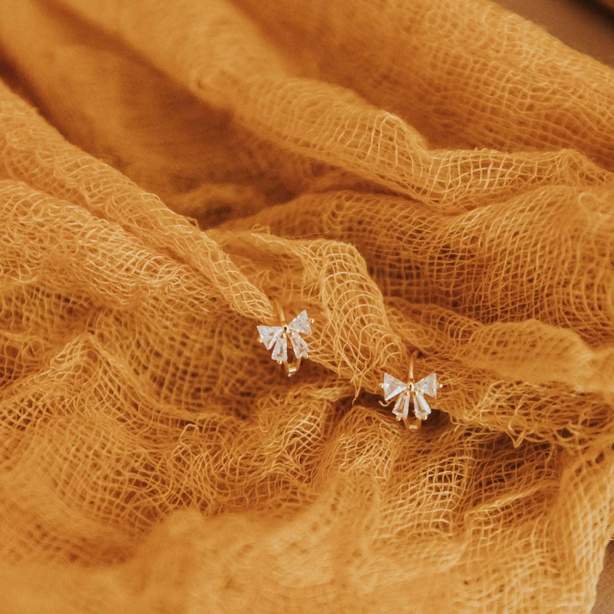 Pair of butterfly-shaped earrings on a textured orange fabric background