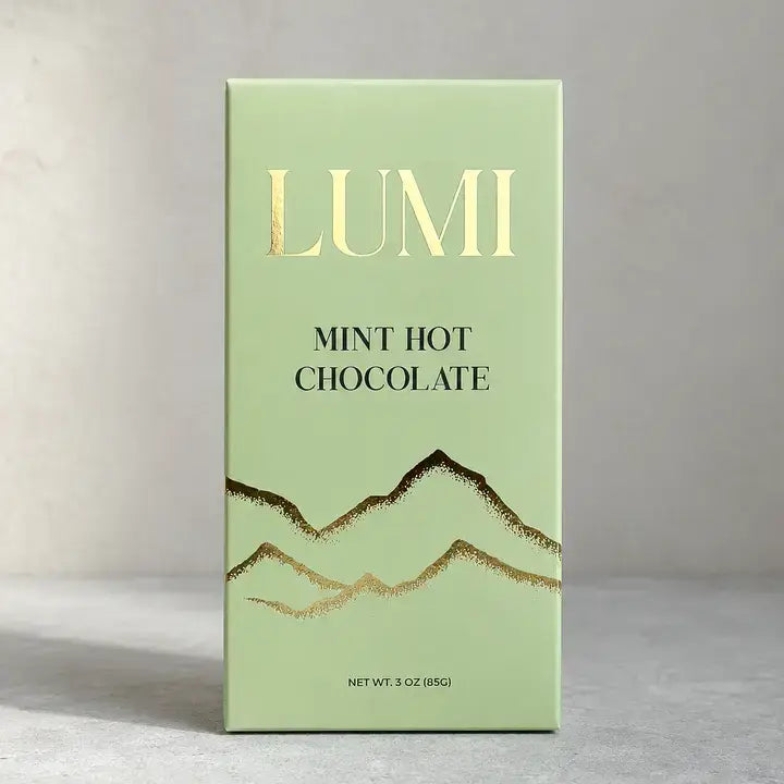 A mint green rectangular box of LUMI Mint Hot Chocolate with gold foil mountain graphics and gold lettering, standing on a light gray surface against a neutral gray background.