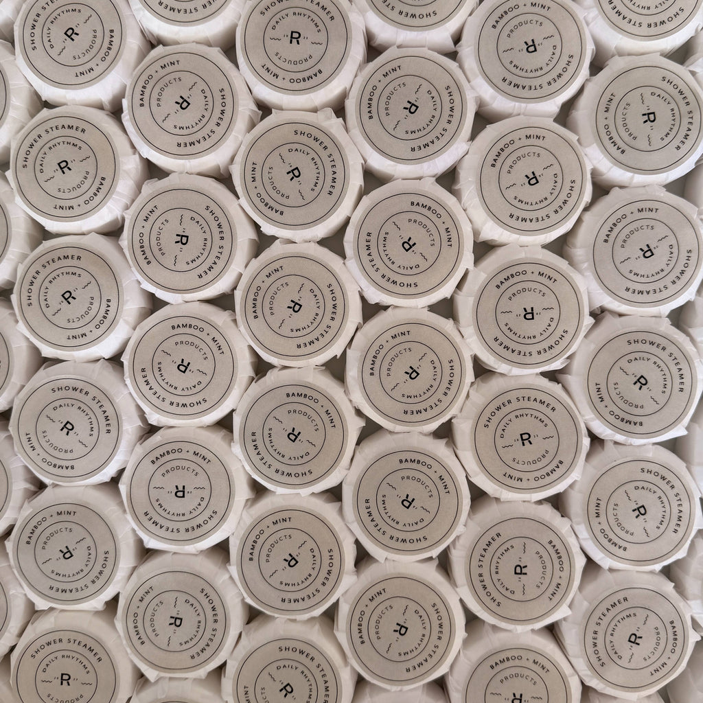 A dense, top-down view of many small white cosmetic jars arranged in a grid, showing the circular white lids with black printed text and a central 'R' logo. The visible text includes 'RUMORS BY R' and 'SOUR APPLE'.
