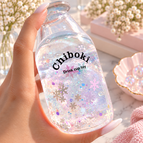 Chiboki Studio Winter Snowflake Sand Bottle Squishy filled with iridescent glitter and pastel snowflake confetti, held by a hand with pale pink nails against a soft pink background with delicate white flowers.