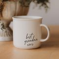 Cream ceramic coffee mug featuring “best grandma ever” in elegant black handwritten script, styled on a warm wooden surface with soft neutral décor and greenery in the background. A thoughtful gift for Grandma for birthdays, Mother’s Day, or just because.