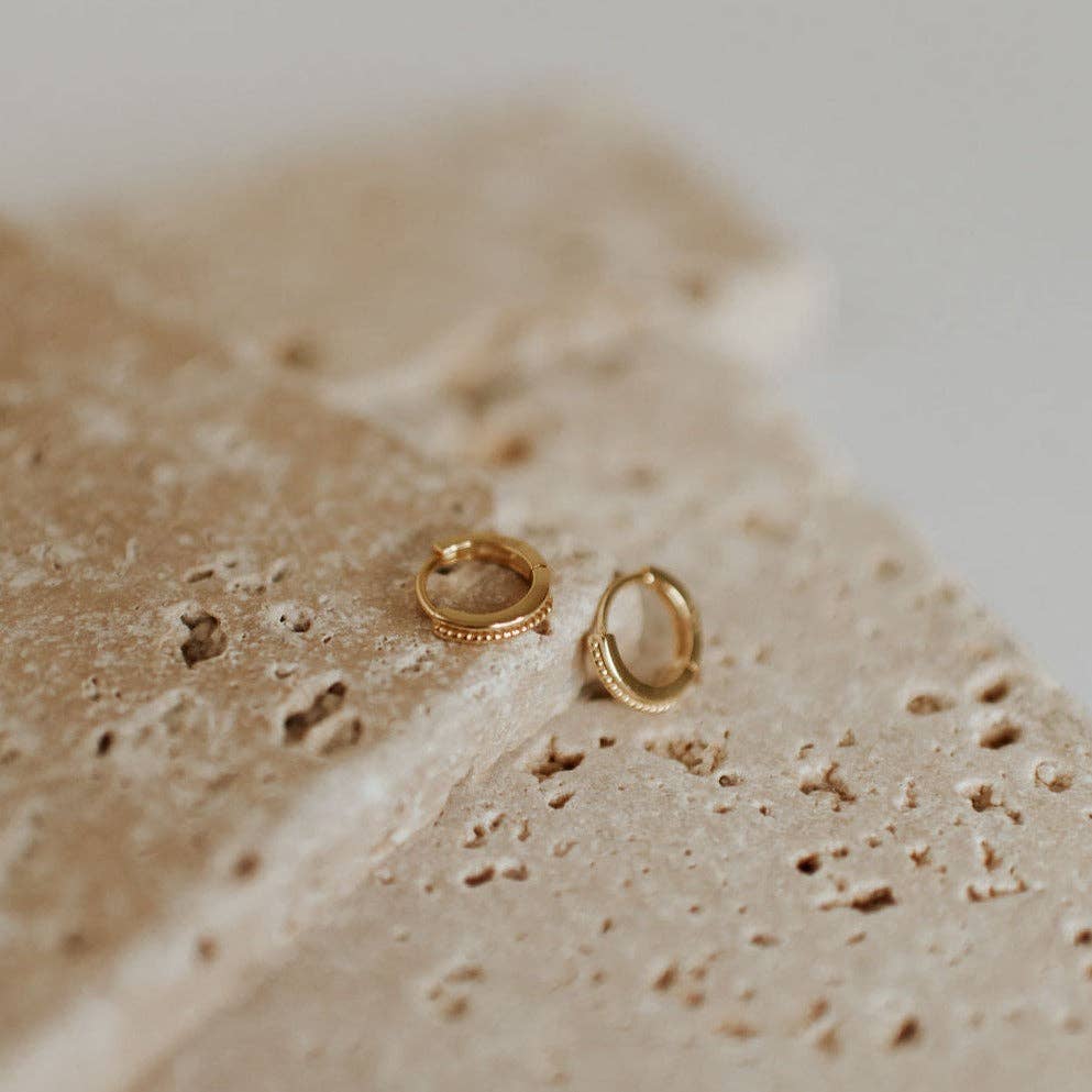 Two gold hoop earrings on a textured beige surface