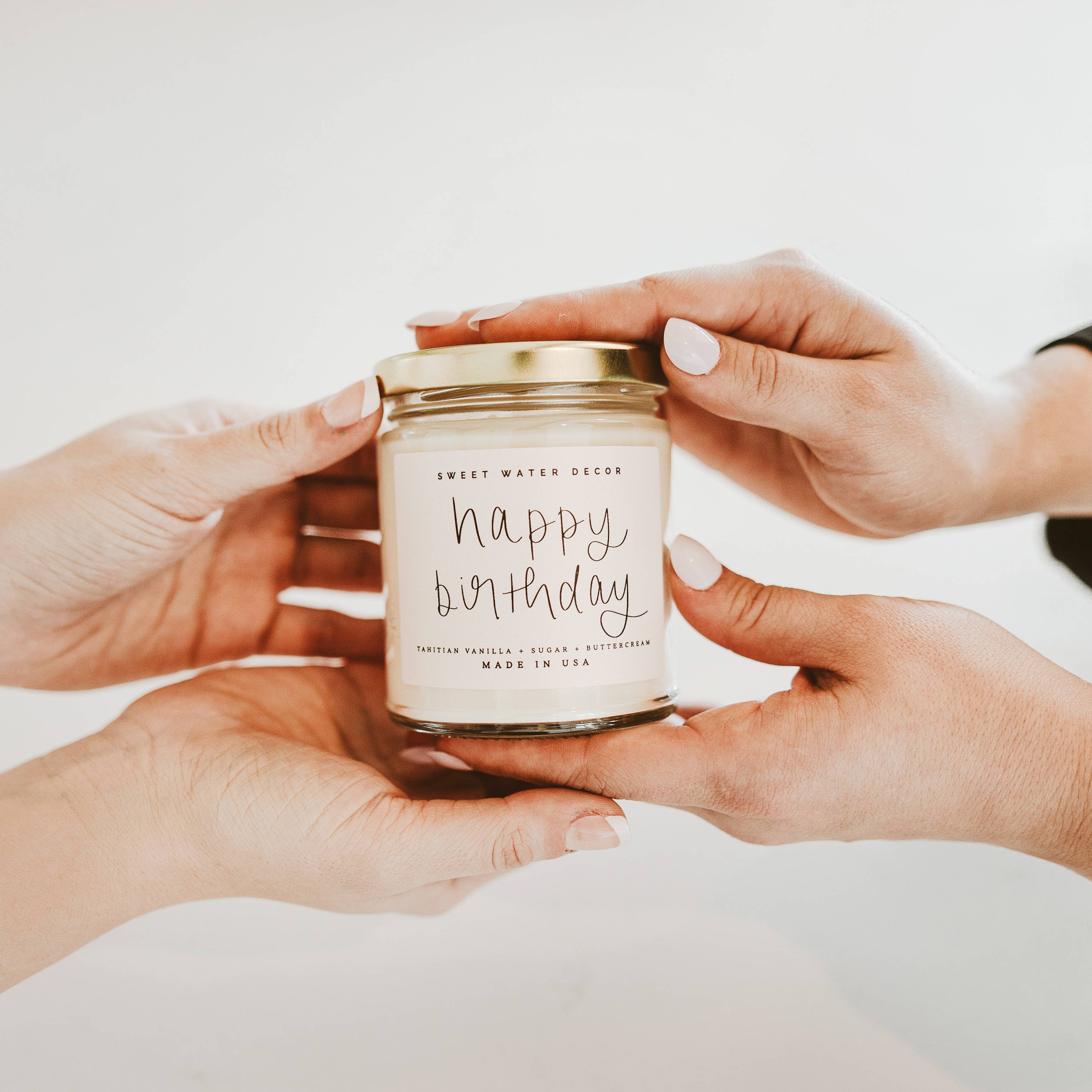 Hands holding a 'Happy Birthday' candle against a plain background