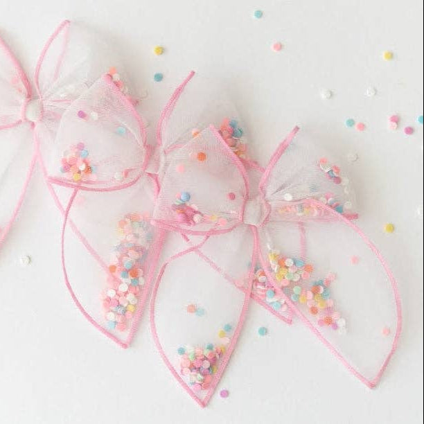 Pink decorative bows with colorful sprinkles on a white background