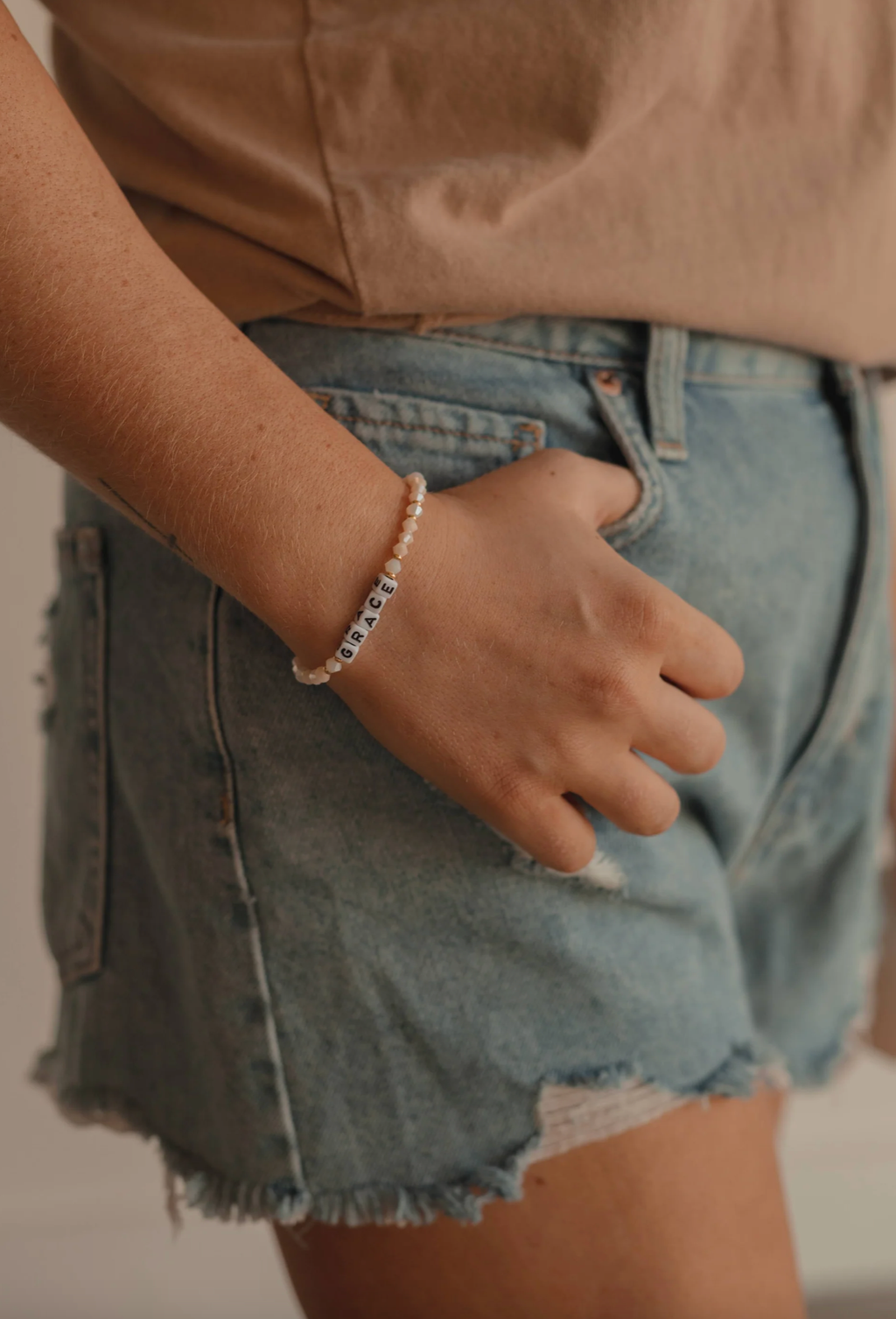 Person wearing a bracelet with denim shorts and a beige top.