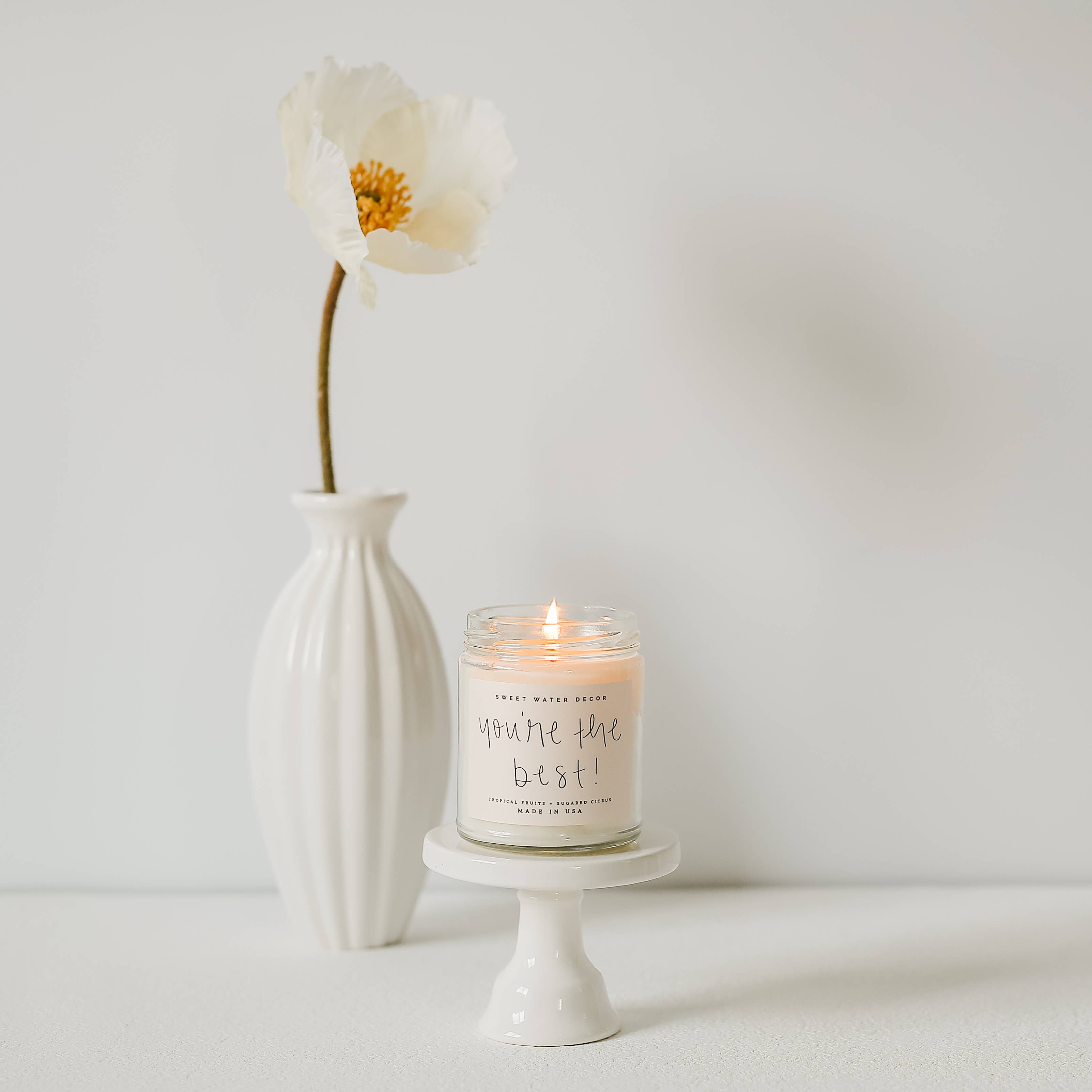 Candle with 'You're the best!' message in a white vase and pedestal on a light background