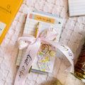 Notebook with a pink ribbon, decorative stickers, and a small bottle on a textured surface.