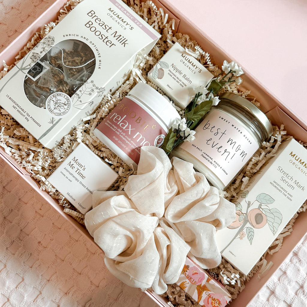 Gift box with breast milk booster, candles, and other items on a textured surface