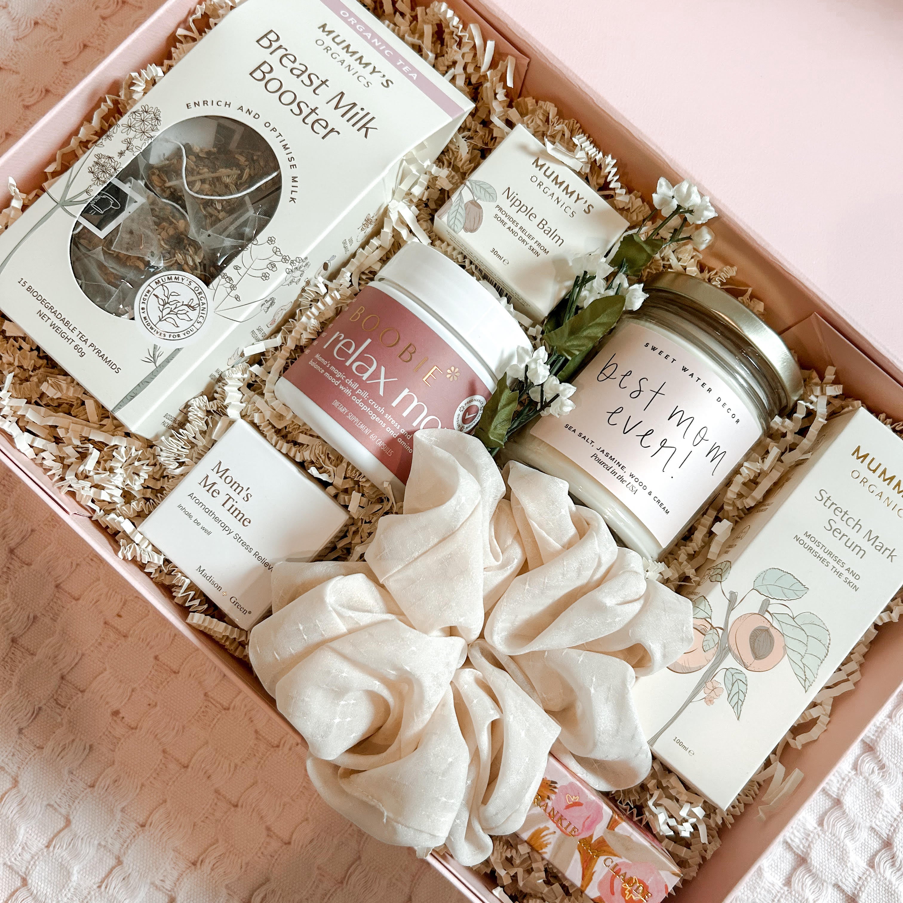 Gift box with breast milk booster, candles, and other items on a textured surface