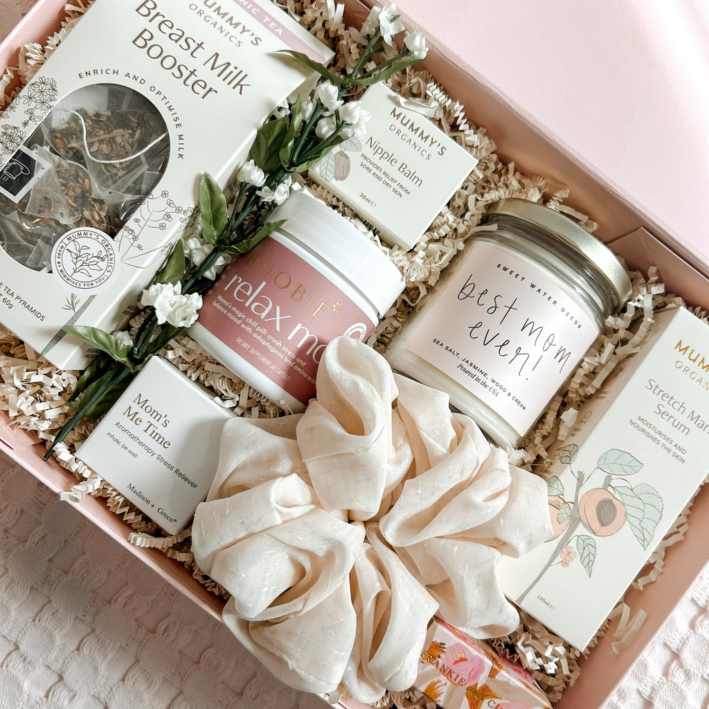 Gift box with breast milk booster, candles, and other items on a textured surface