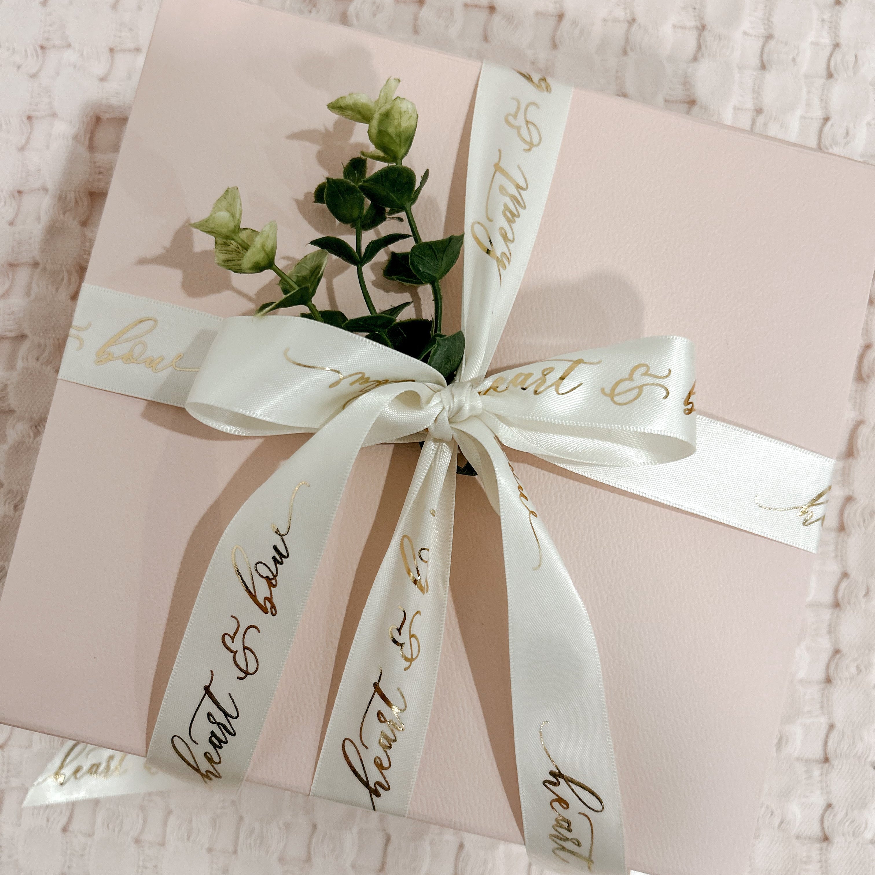 Gift box with a white ribbon and greenery on a textured surface