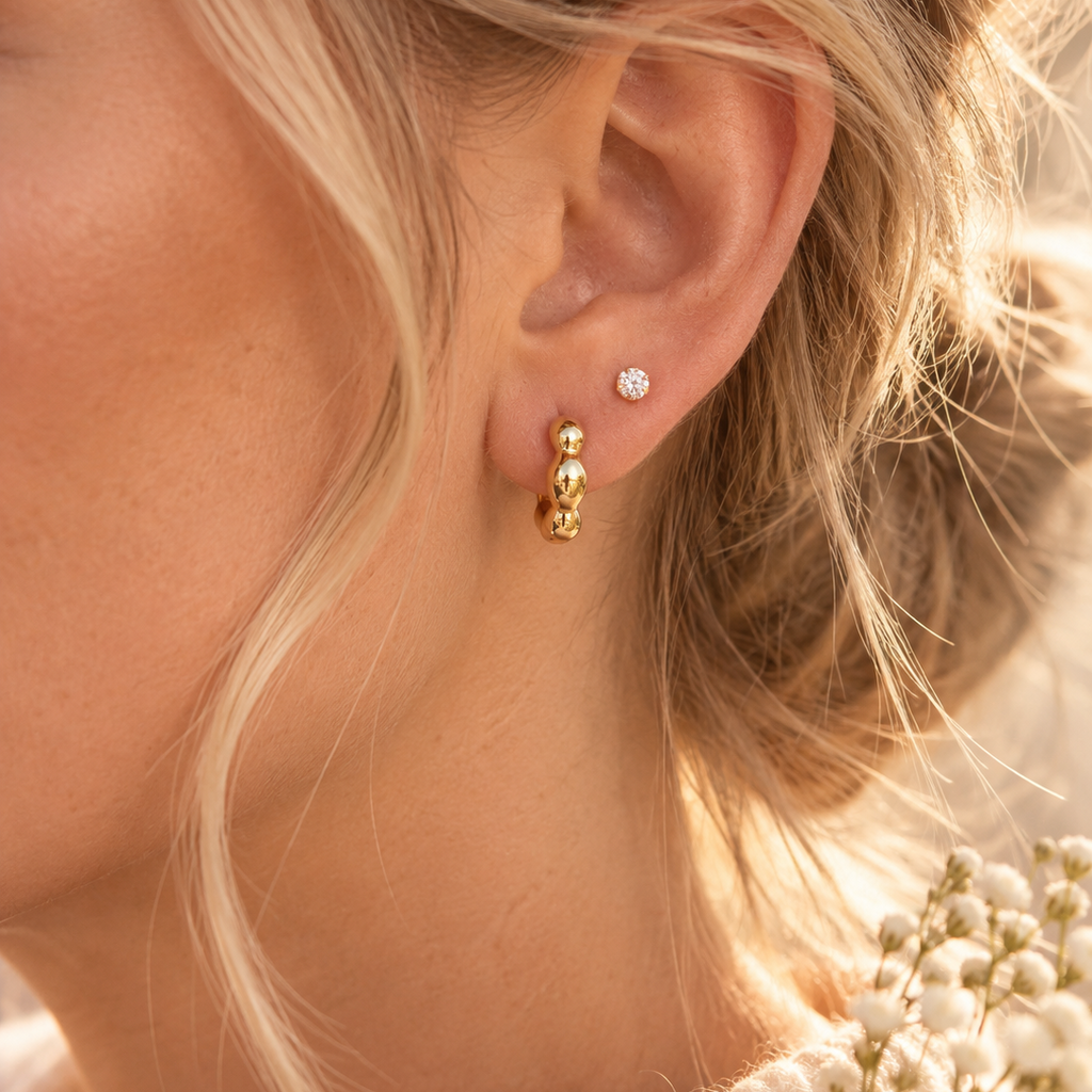 Blaire gold bubble huggie earrings worn on ear with a delicate crystal stud.