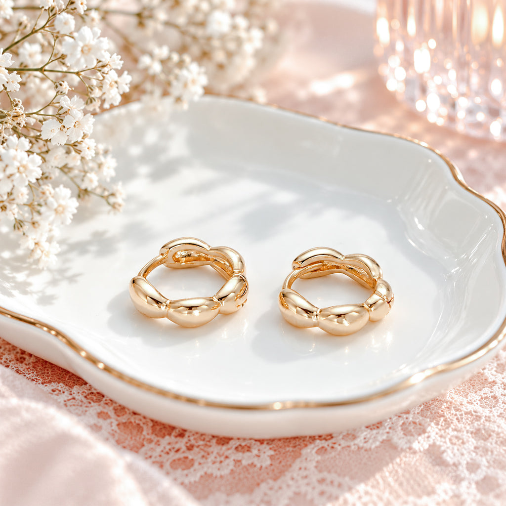Blaire gold bubble huggie earrings styled on a white jewelry dish with blush pink lace.