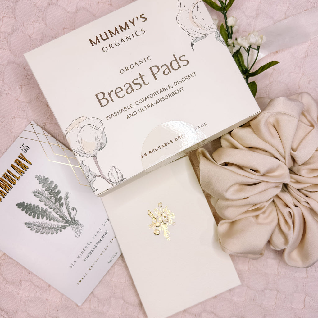 Mummy's Organics breast pads packaging on a pink background with flowers and a scrunchie.