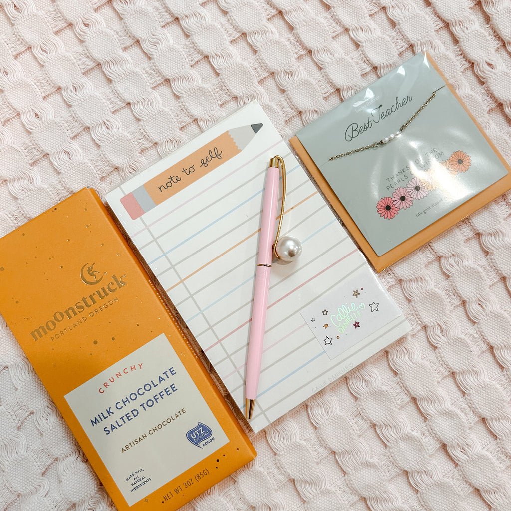 Chocolate bar, notepad, pen, and necklace on a textured surface