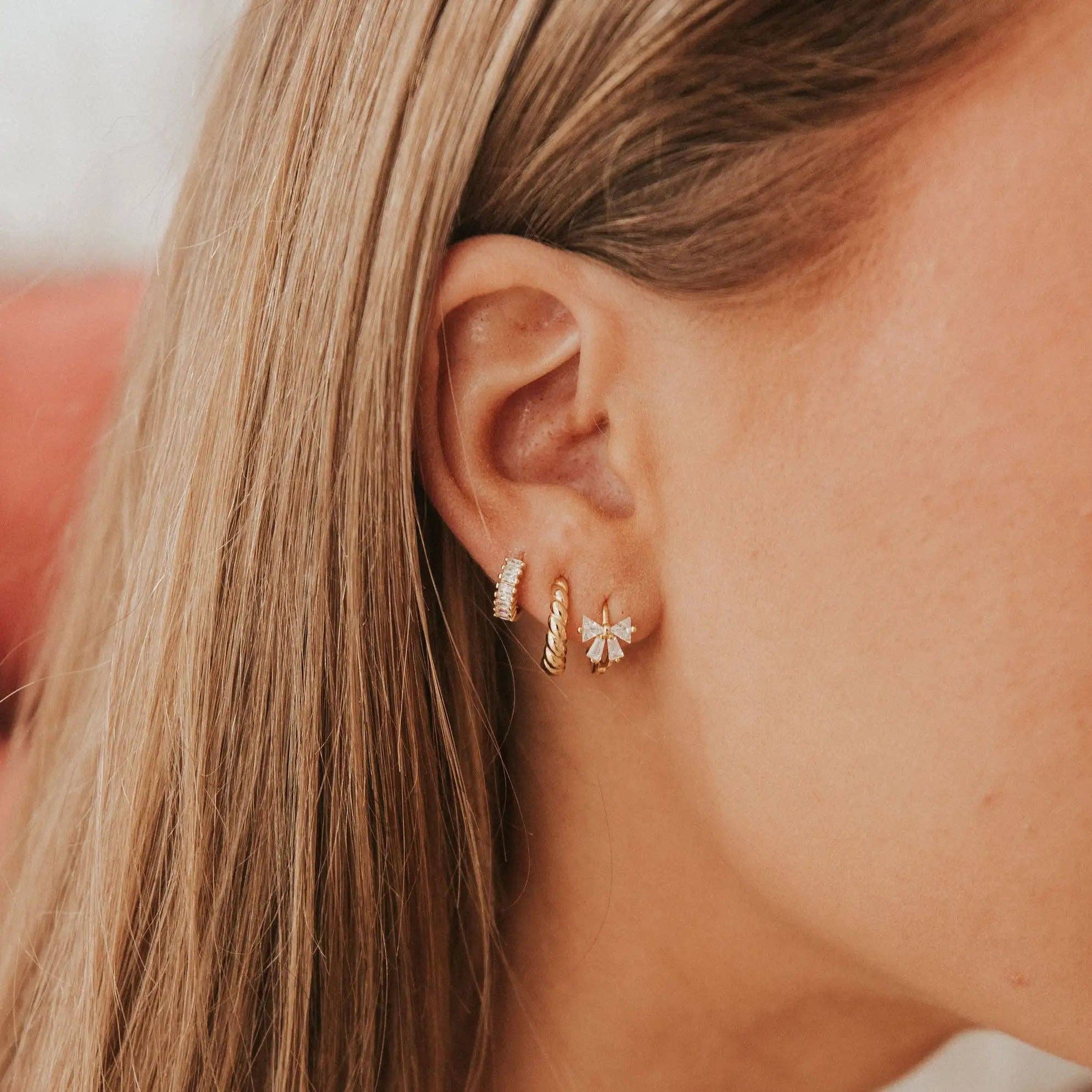 Close-up of a person wearing gold and silver earrings with a neutral background