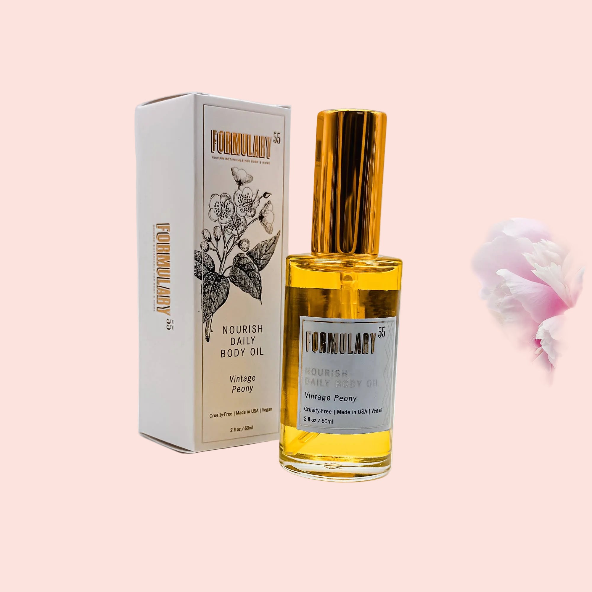 Body oil bottle with gold cap and white label next to its packaging on a light gray background with pink flowers.