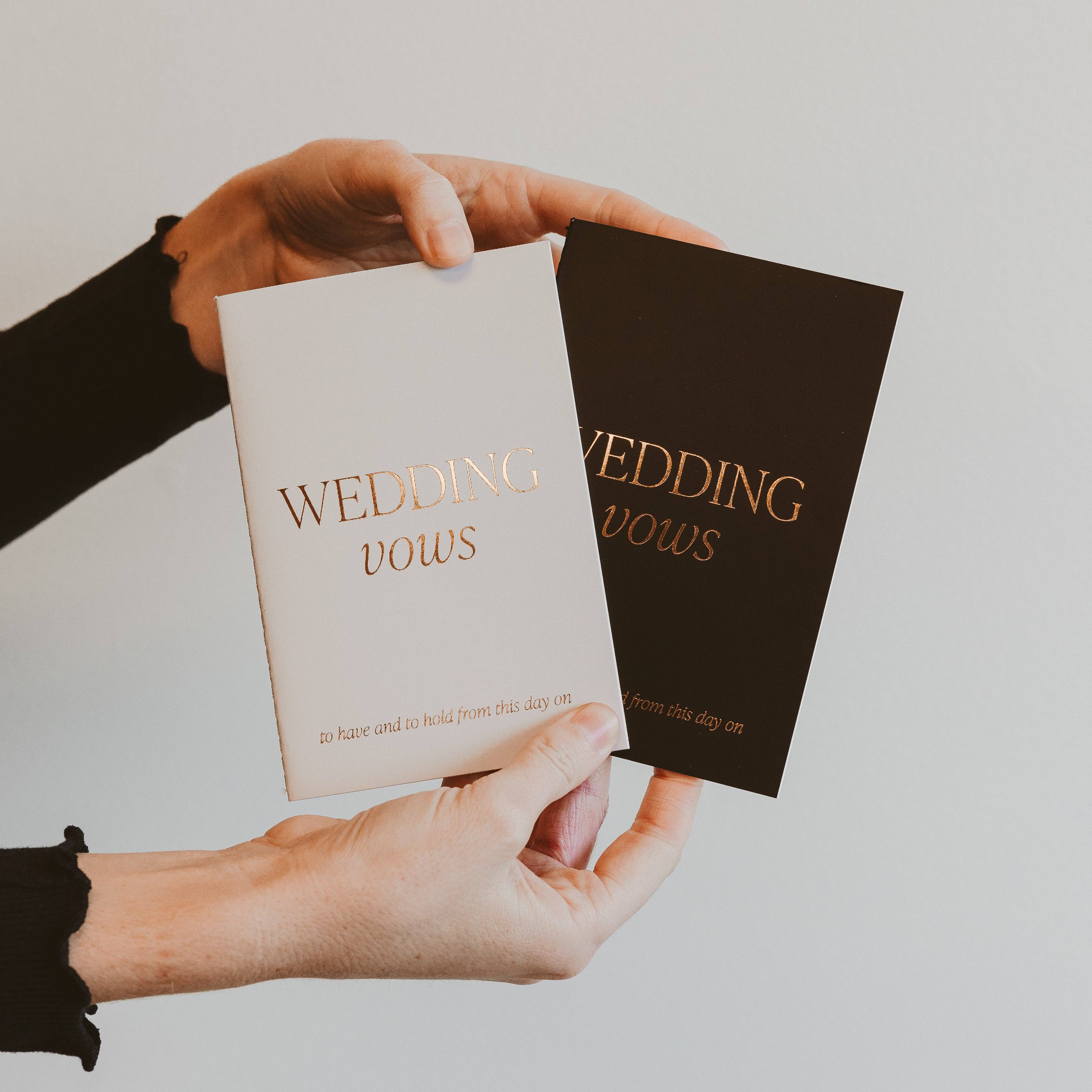 Two wedding vow books held by a person against a plain background