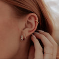 Close-up of a person wearing gold hoop earrings with a blurred background