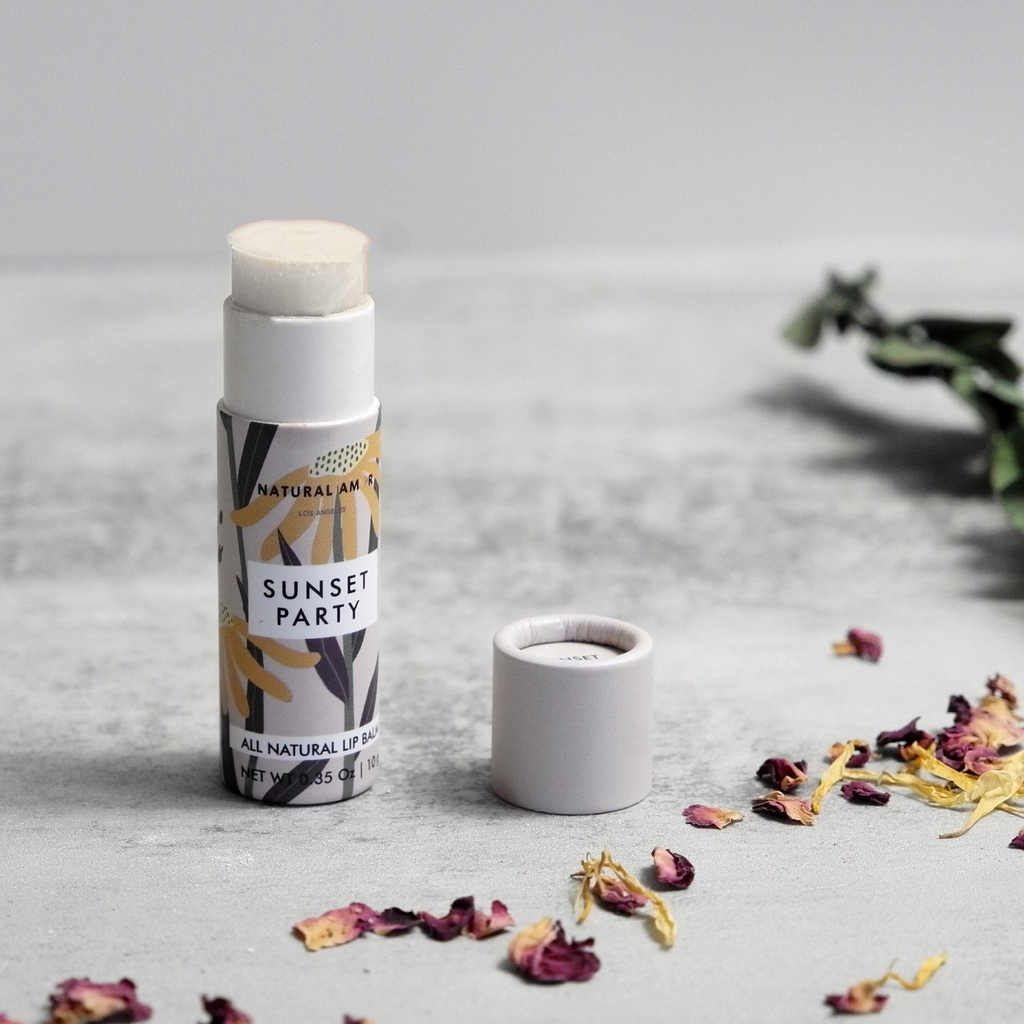 Lip balm with packaging labeled 'Sunset Party' on a light surface with dried flowers.