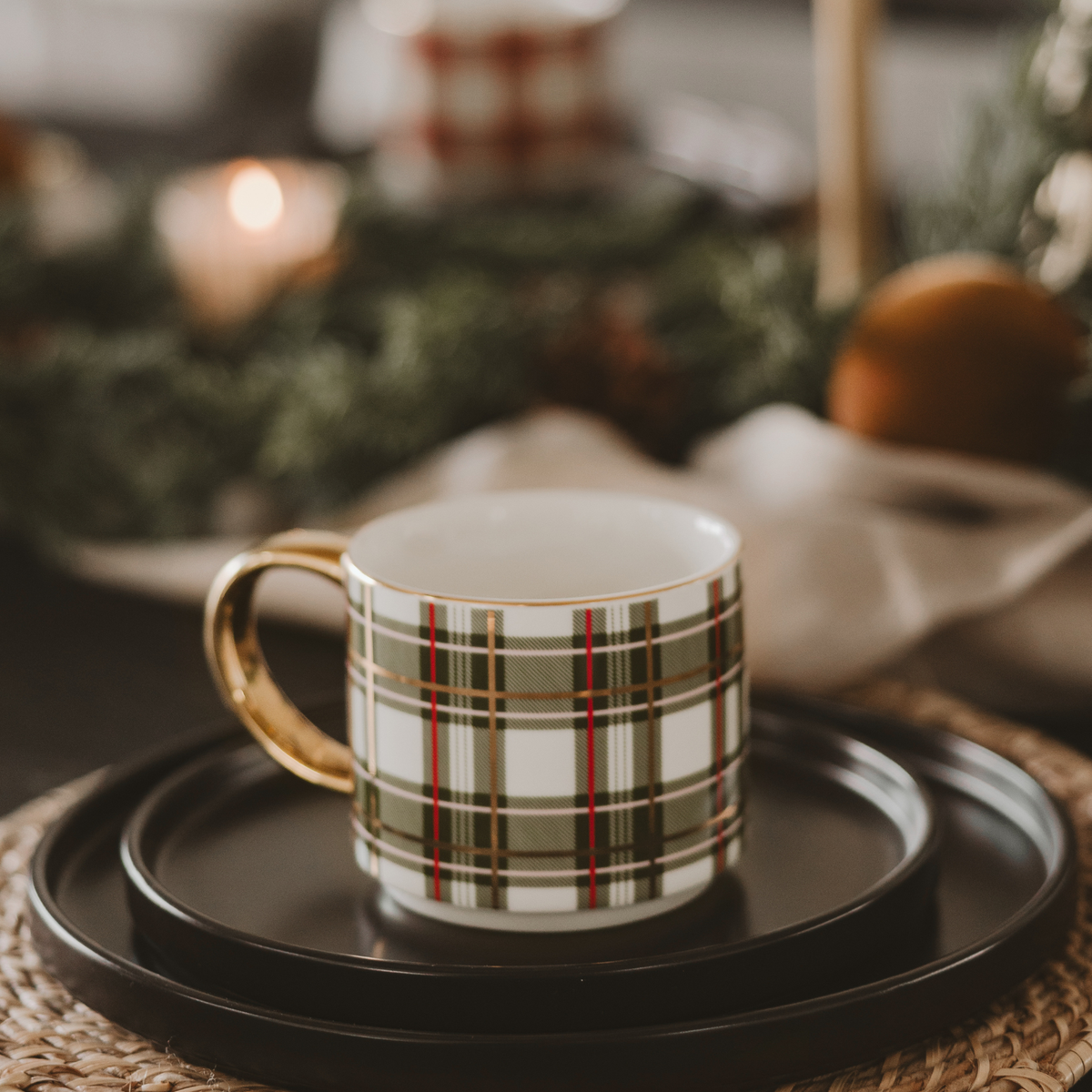Green plaid Christmas coffee mug with a gold handle on stacked black plates at a festive table setting.
