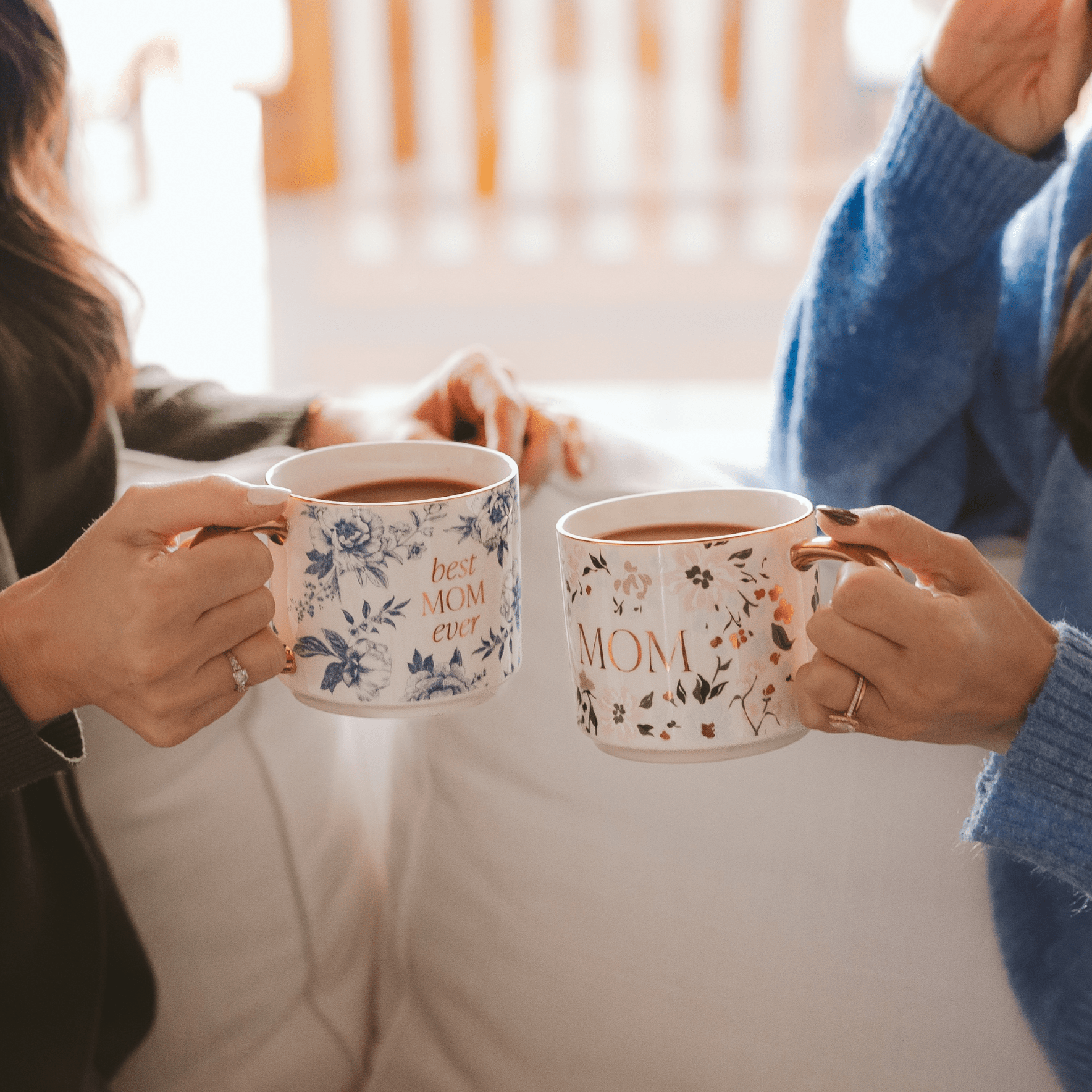 Two people holding mugs with 'mom' and 'best mom ever' text in a cozy setting.