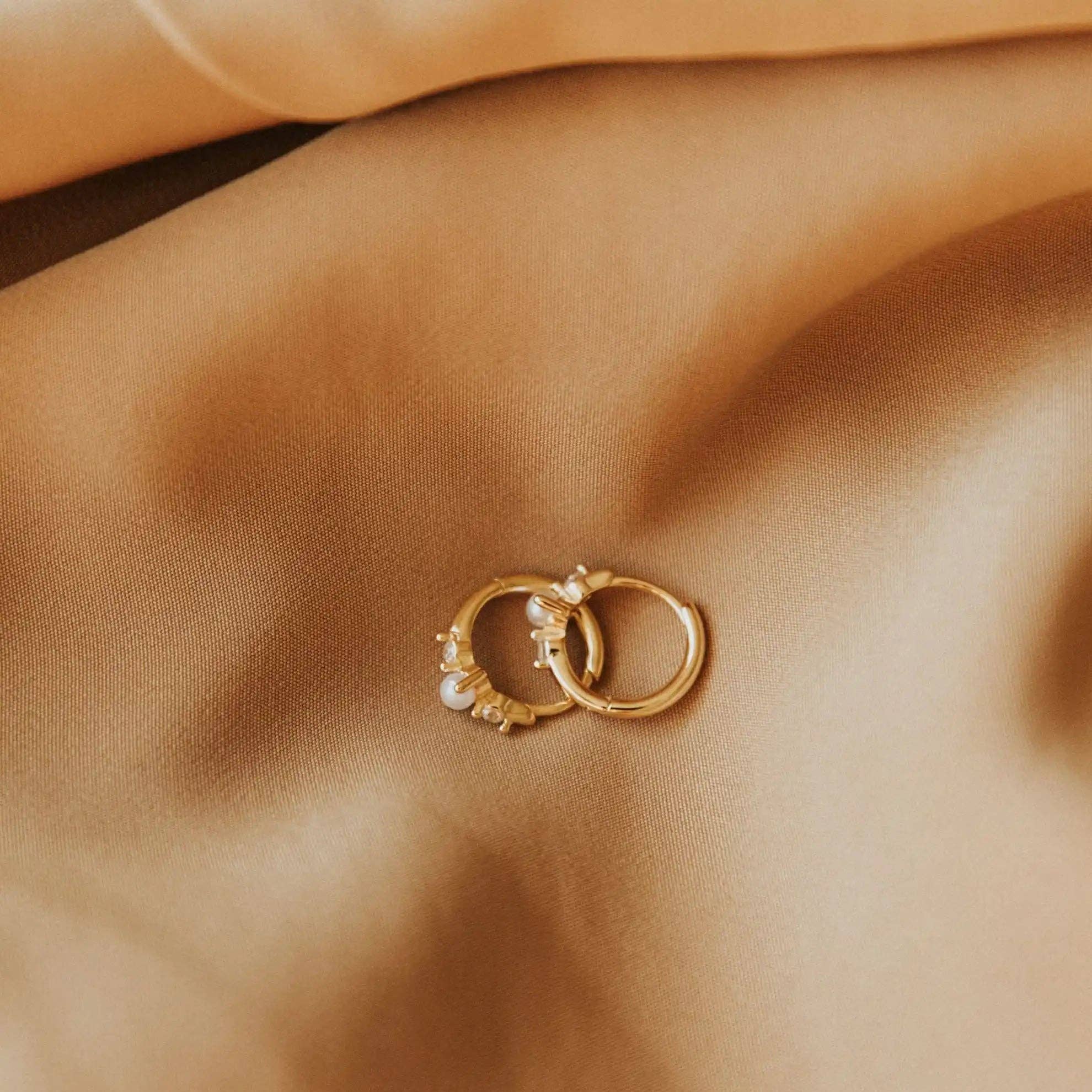 Pair of gold hoop earrings with small pearls on a beige fabric background