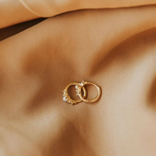 Pair of gold hoop earrings with small pearls on a beige fabric background