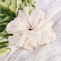 White scrunchie on a textured white surface with green leafy background